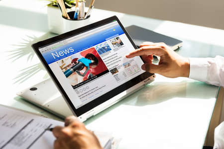 Businessman s hand checking online news on laptop over reflective desk Stock Photo
