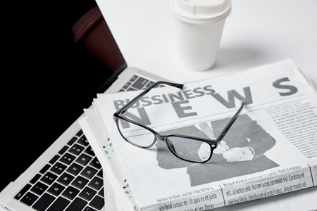 Laptop with blank screen near business newspapers glasses paper cup and pen on white