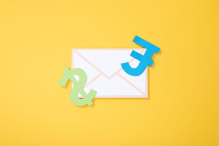 Top view of paper icons of envelope and types of currency on yellow Stock Photo