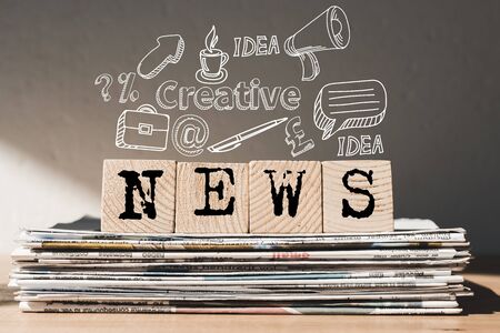 Wooden blocks with black news lettering on pile of newspapers with idea icons above