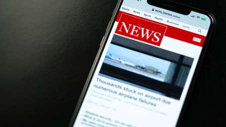 Online news on a smart phone businessman reading news or article on a mobile phone screen app hand holding smart device newspaper and portal on internet displayed news are not reality related Stock Photo