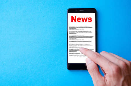 News reading the news the inscription red news on the smartphone screen lies on a blue background male hand holds a smartphone clicks leafs through the news