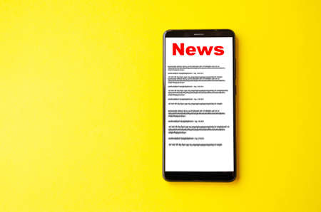 News reading the news the inscription red news on the smartphone screen lies on a yellow background male hand holds a smartphone clicks leafs through the news