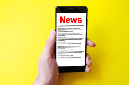 News reading the news the inscription red news on the smartphone screen lies on a yellow background male hand holds a smartphone clicks leafs through the news