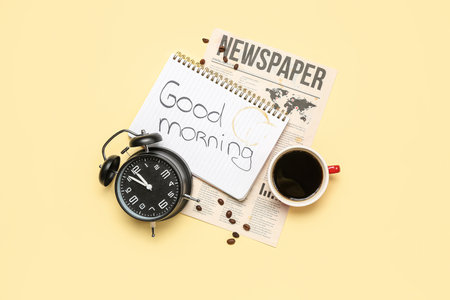 Notebook with text good morning alarm clock cup of coffee and newspaper on color background Stock Photo