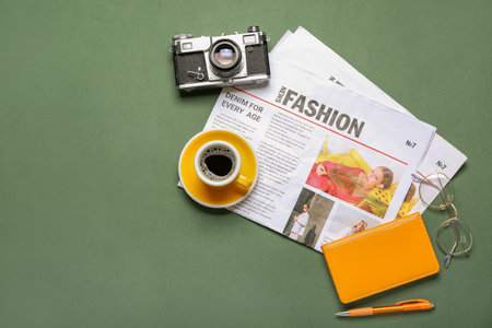 Newspapers with cup of coffee photo camera eyeglasses and notebook on green background