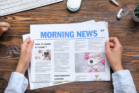 Woman reading newspaper at workplace on wooden background