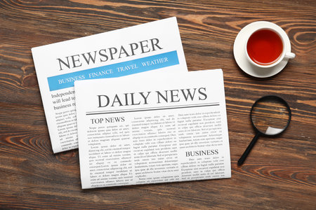 Newspapers with magnifying glass and cup of tea on wooden background Stock Photo