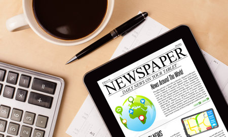 Workplace with tablet pc showing news and a cup of coffee on a wooden work table close up Stock Photo