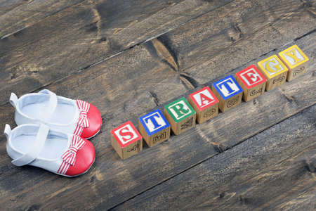 Kid shoes and word strategy on wooden table Stock Photo