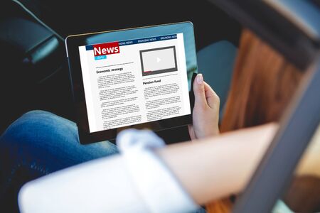 Young beautiful woman sitting in the back seat of a car with a tablet in hands Stock Photo